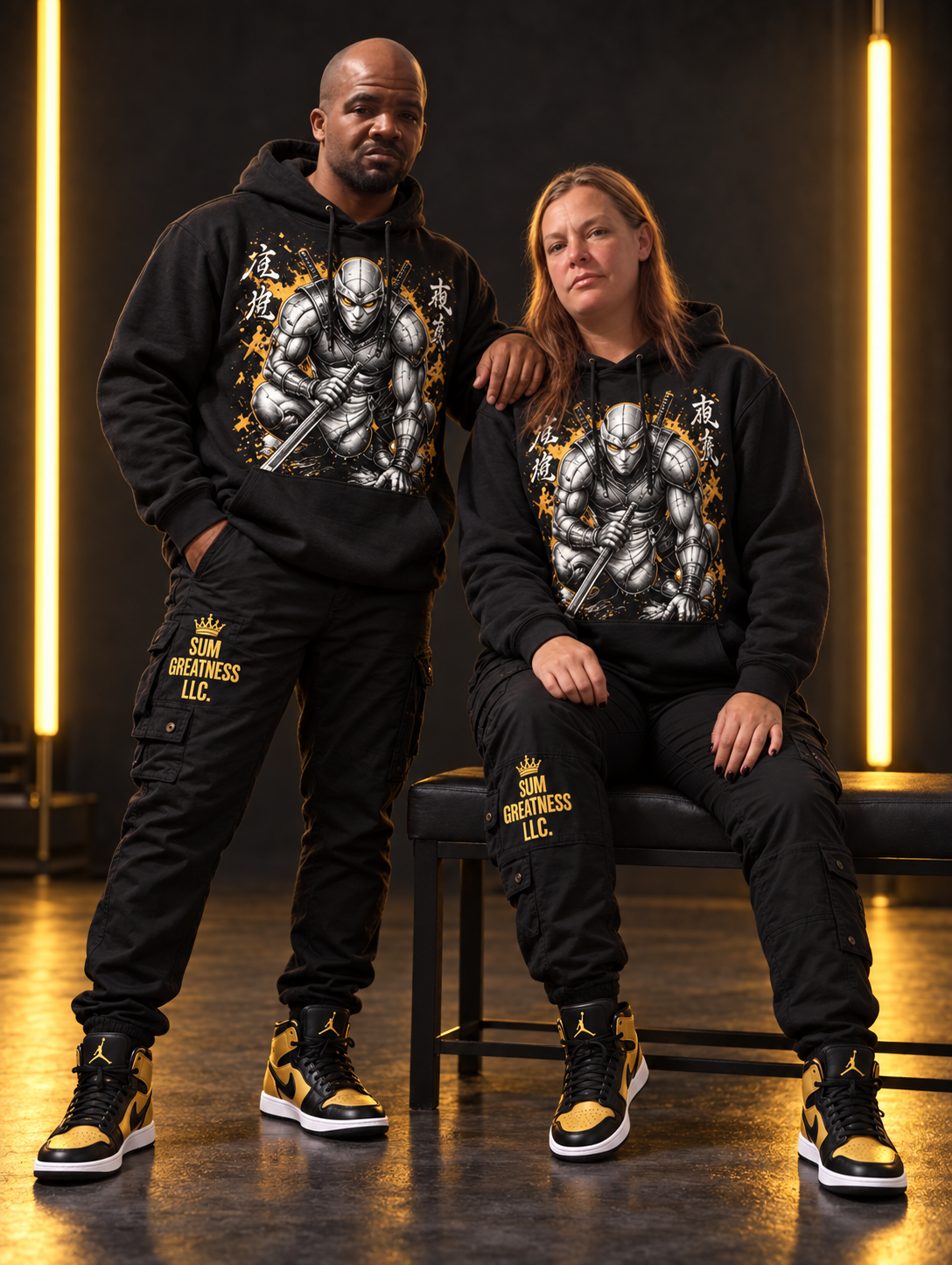 Kevin standing beside his seated wife in black and gold artwork hoodie outfits